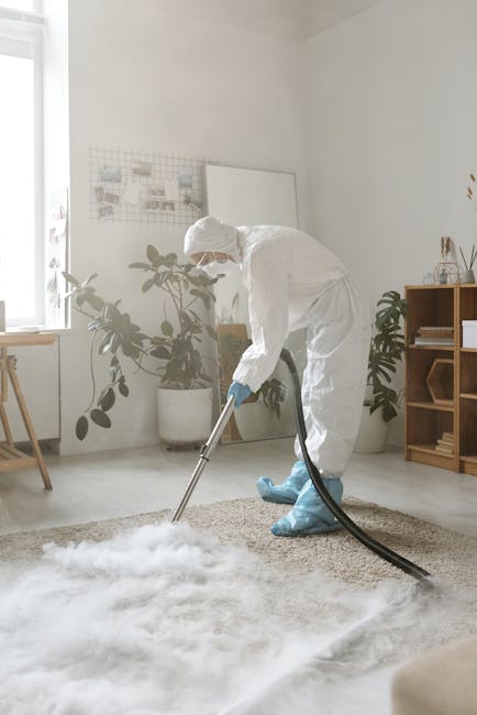 Close-up of a vacuum cleaner head actively cleaning an ornate, patterned carpet in a residential setting, with the user in casual clothing visible in the background. The carpet features intricate flor